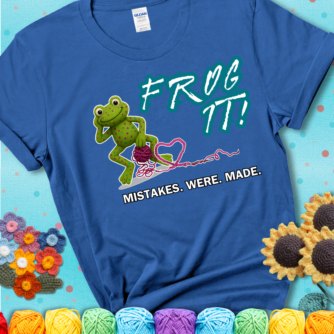 Green frog with yarn and heart-shaped loop. Text reads: “Frog It! Mistakes Were Made.” A playful crochet tee for anyone who's ever had to rip it back, showing a blue tee with a teal sunflower background