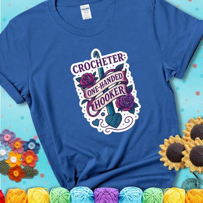 Royal blue t-shirt with a tattoo-style crochet design featuring a crochet hook, roses, and the phrase “Crocheter: One-Handed Hooker.”