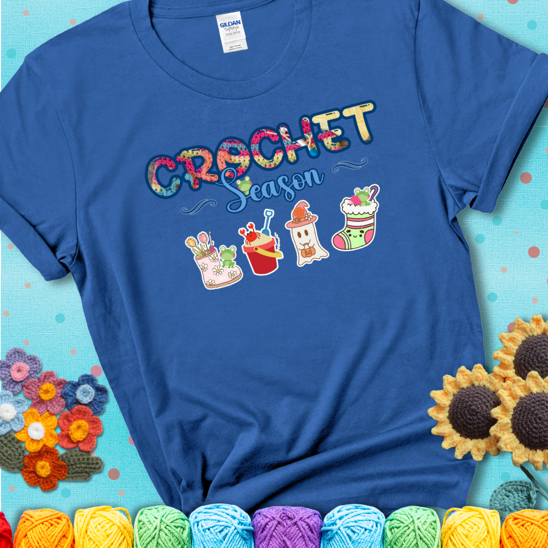Blue t-shirt shows the words “Crochet Season” with cute seasonal icons below: a spring boot with hooks, summer bucket with crab, fall ghost with pumpkin hat, winter stocking, and tiny frogs.