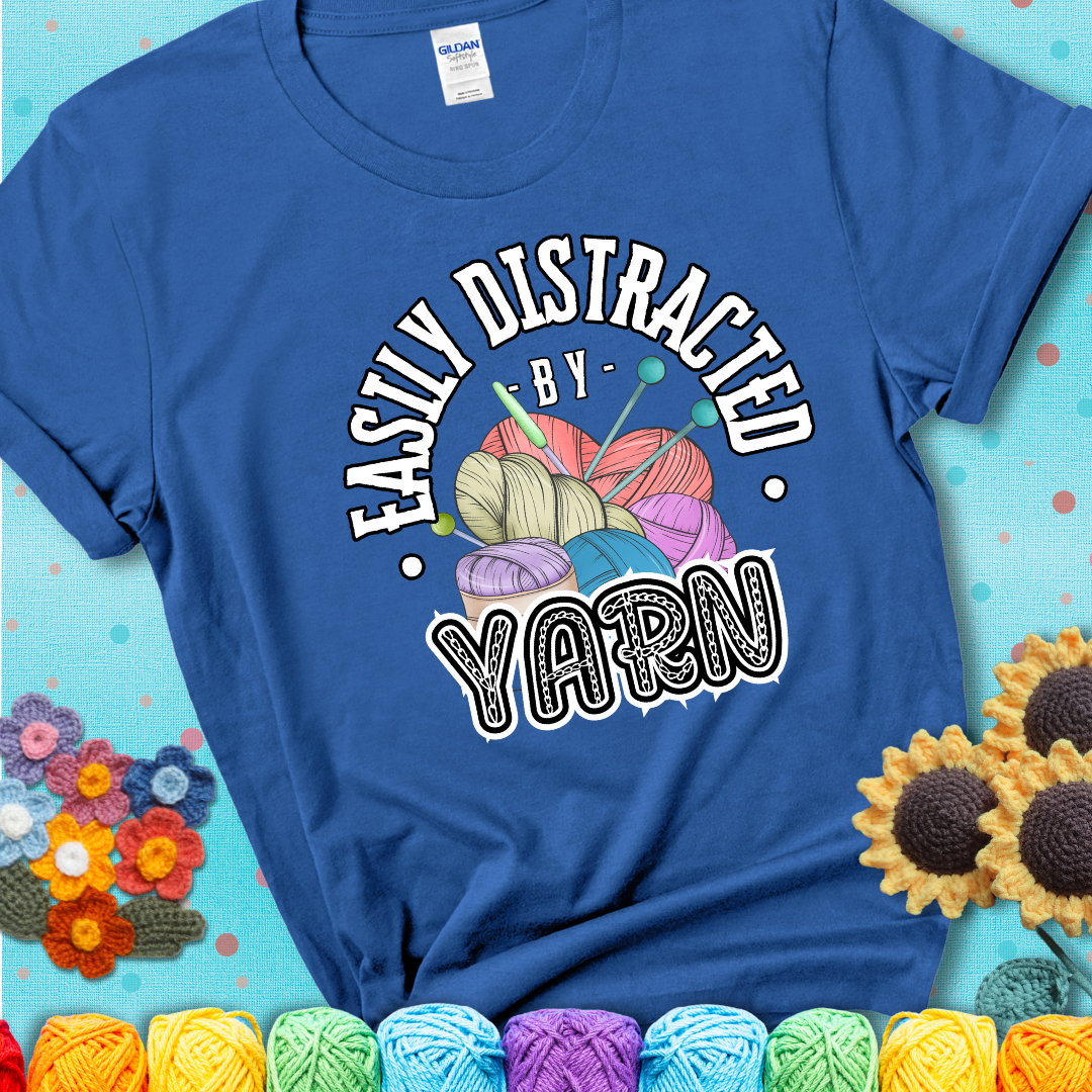If yarn steals your focus every Design reads 'Easily Distracted By Yarn', perfect crochet gift for yarn lovers; showing a blue tee with a teal sunflower background