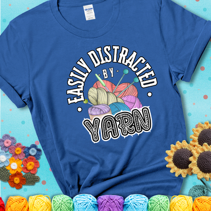 If yarn steals your focus every Design reads 'Easily Distracted By Yarn', perfect crochet gift for yarn lovers; showing a blue tee with a teal sunflower background
