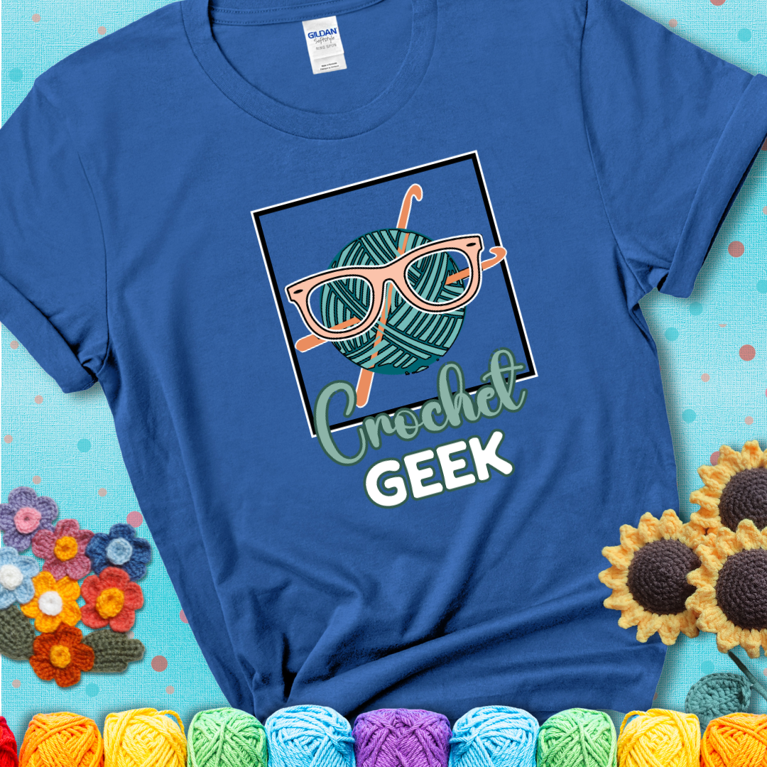 A teal yarn ball with crisscrossed hooks wears oversized nerdy glasses with the phrase “Crochet Geek” in bold, fun text below on a blue t-shirt.