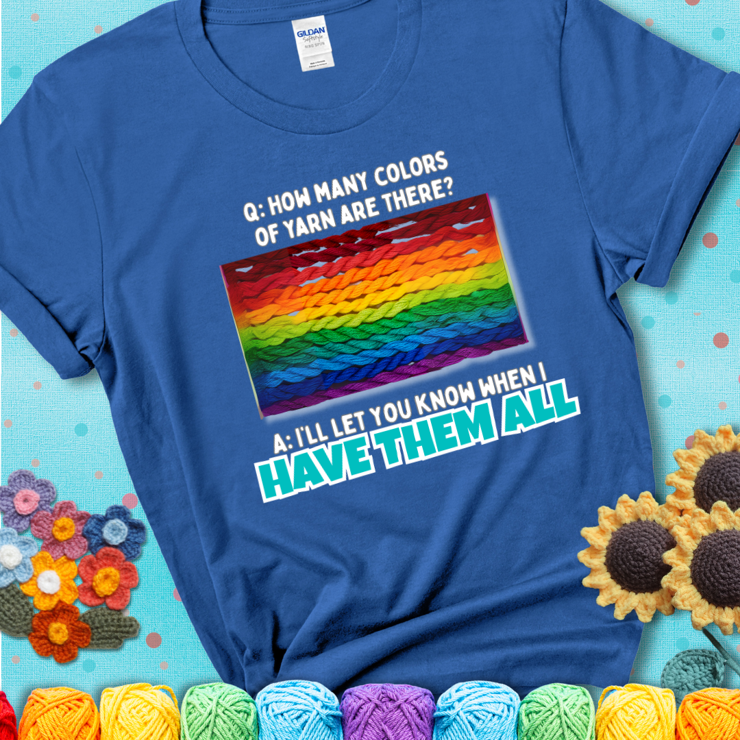 Blue t-shirt with rainbow skeins of yarn stacked in color gradient with playful question: “How many colors of yarn are there?” Answer: “I'll let you know when I have them all.”