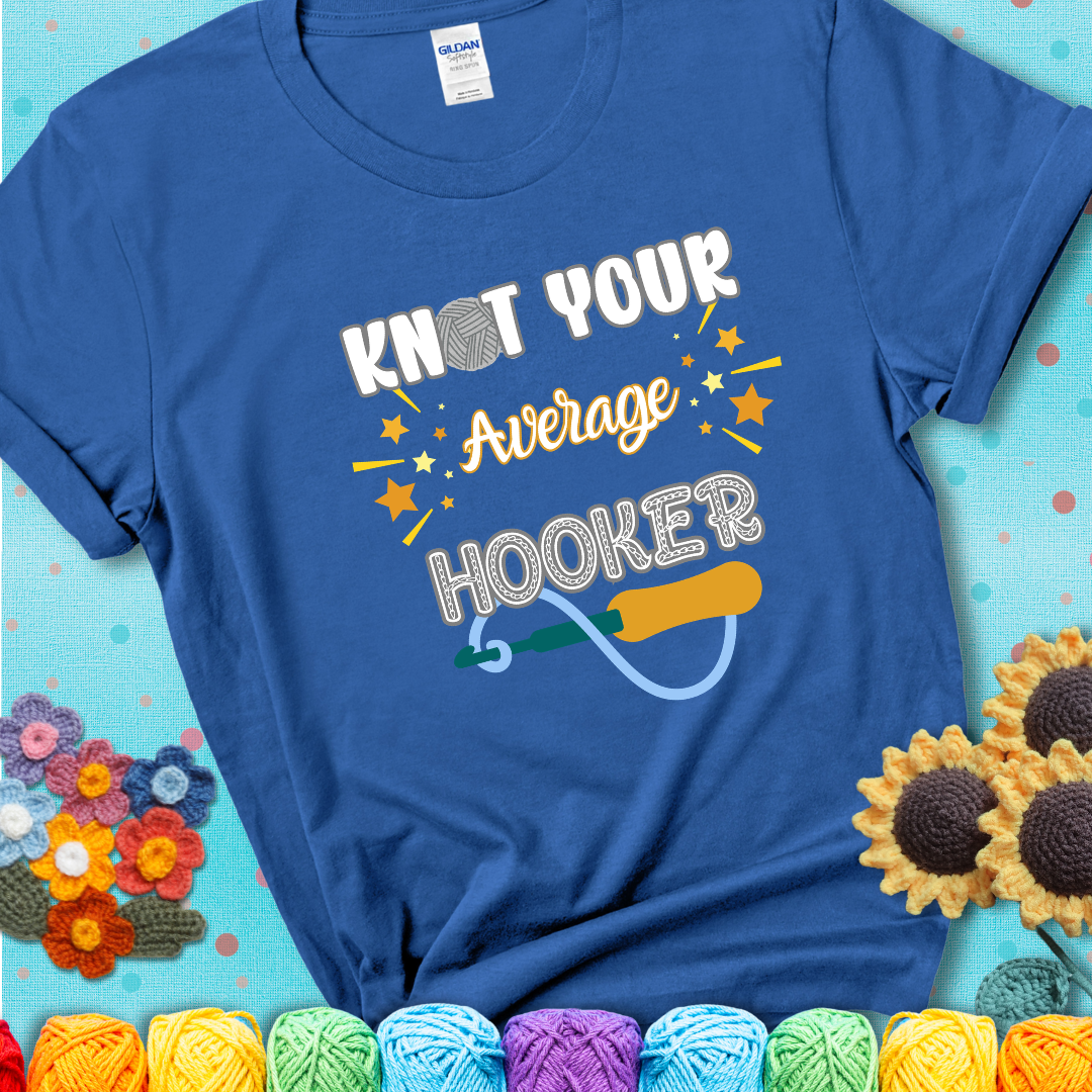 Bold lettering on a blue t-shirt with a yarn hook graphic. Text reads: “I'm Not Your Average Hooker.” A cheeky crochet tee for confident crafters who own their skills.