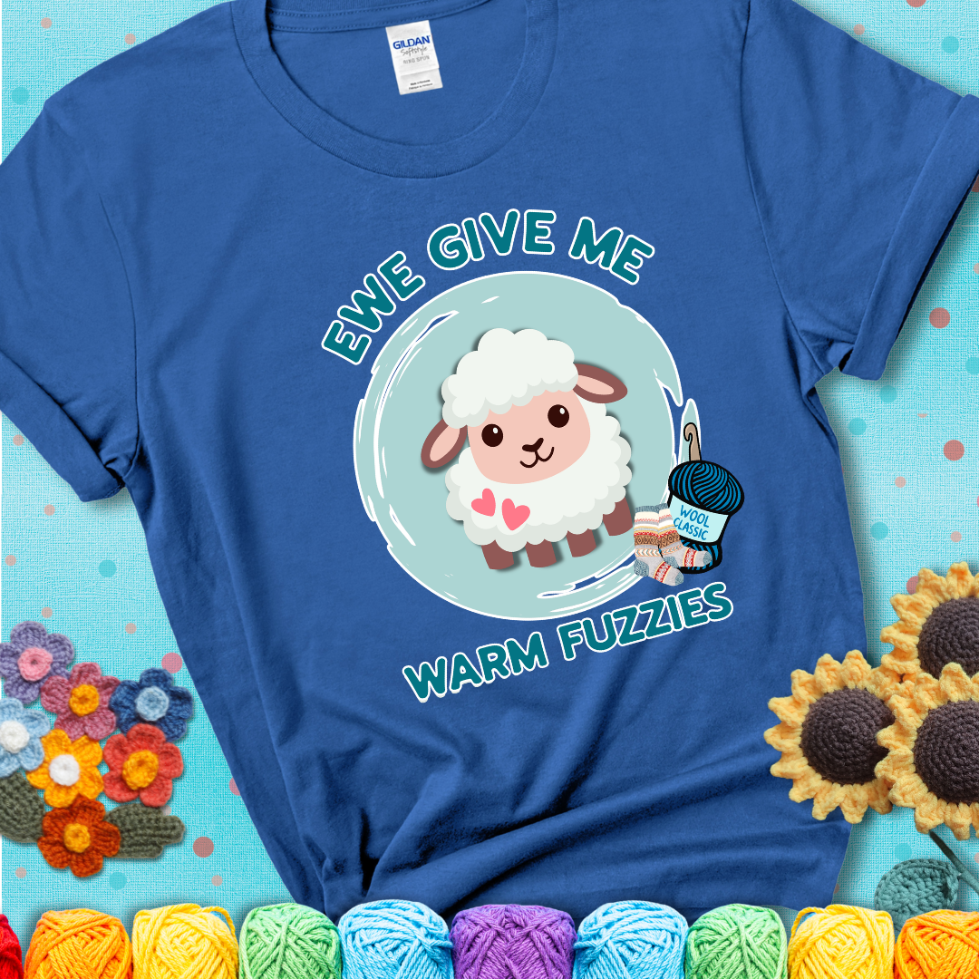 Blue  t-shirt showing a cartoon sheep with pink hearts, wool socks, and yarn labeled “Wool Classic.” Text reads “Ewe Give Me Warm Fuzzies.”