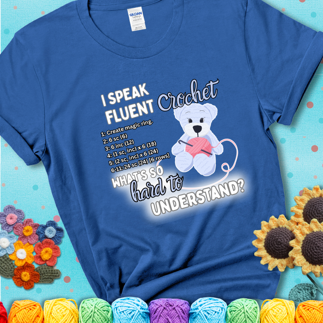 A cute crochet bear holding a yarn ball, surrounded by a short crochet pattern. The phrase reads “I Speak Fluent Crochet – What’s so hard to understand?” on a blue t-shirt.