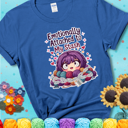 Adorable character with wide eyes hugging a yarn stash wrapped in chains and a lock, with the text “Emotionally Attached to My Stash”  on a blue tee.