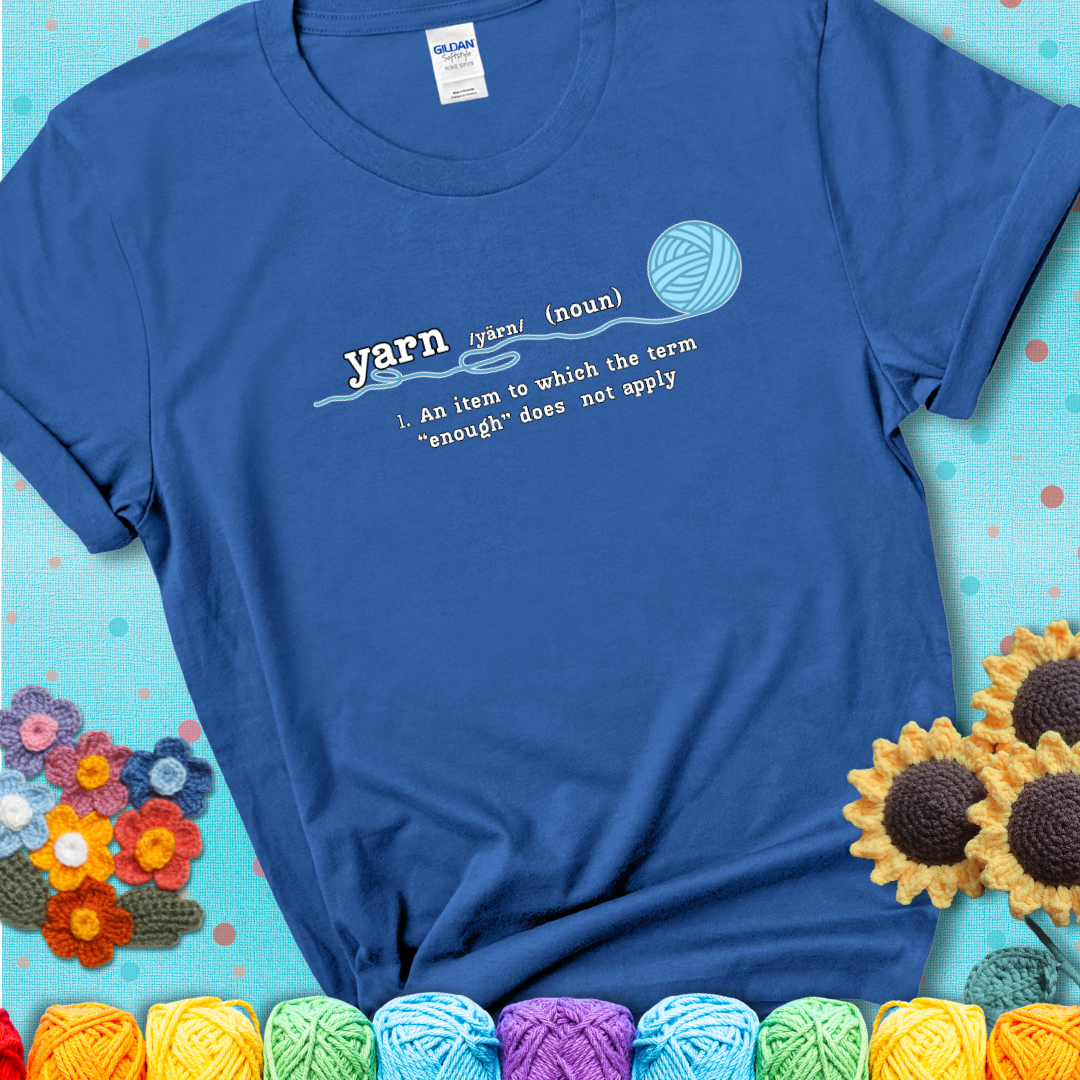 Royal blue t-shirt with a definition-style yarn graphic reading “An item to which the word ‘enough’ does not apply,” plus a blue ball of yarn with a loose strand.