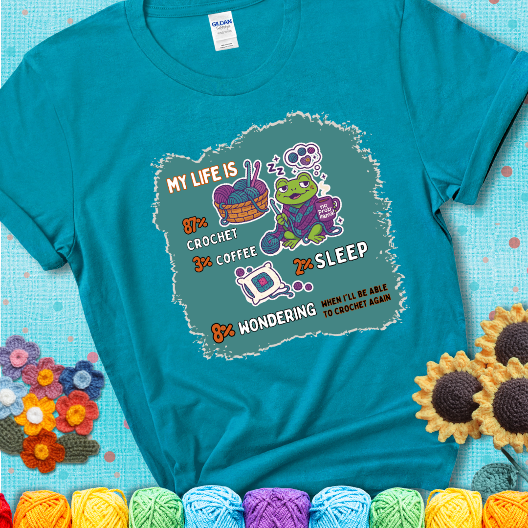 Tropical blue t-shirt with a crocheting frog, coffee, yarn, and text showing a playful life breakdown: 87% crochet, 3% coffee, 2% sleep, 8% wondering when to crochet again.