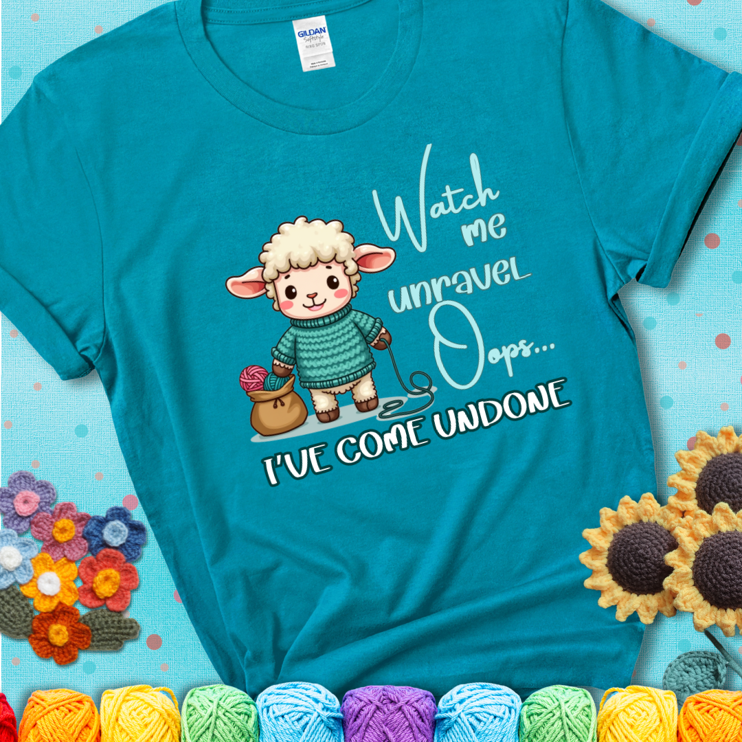 Teal t-shirt with a cute sheep holding yarn looks startled with the phrase “Watch me unravel… Oops, I’ve come undone.” Perfect mix of whimsy and yarn life chaos.