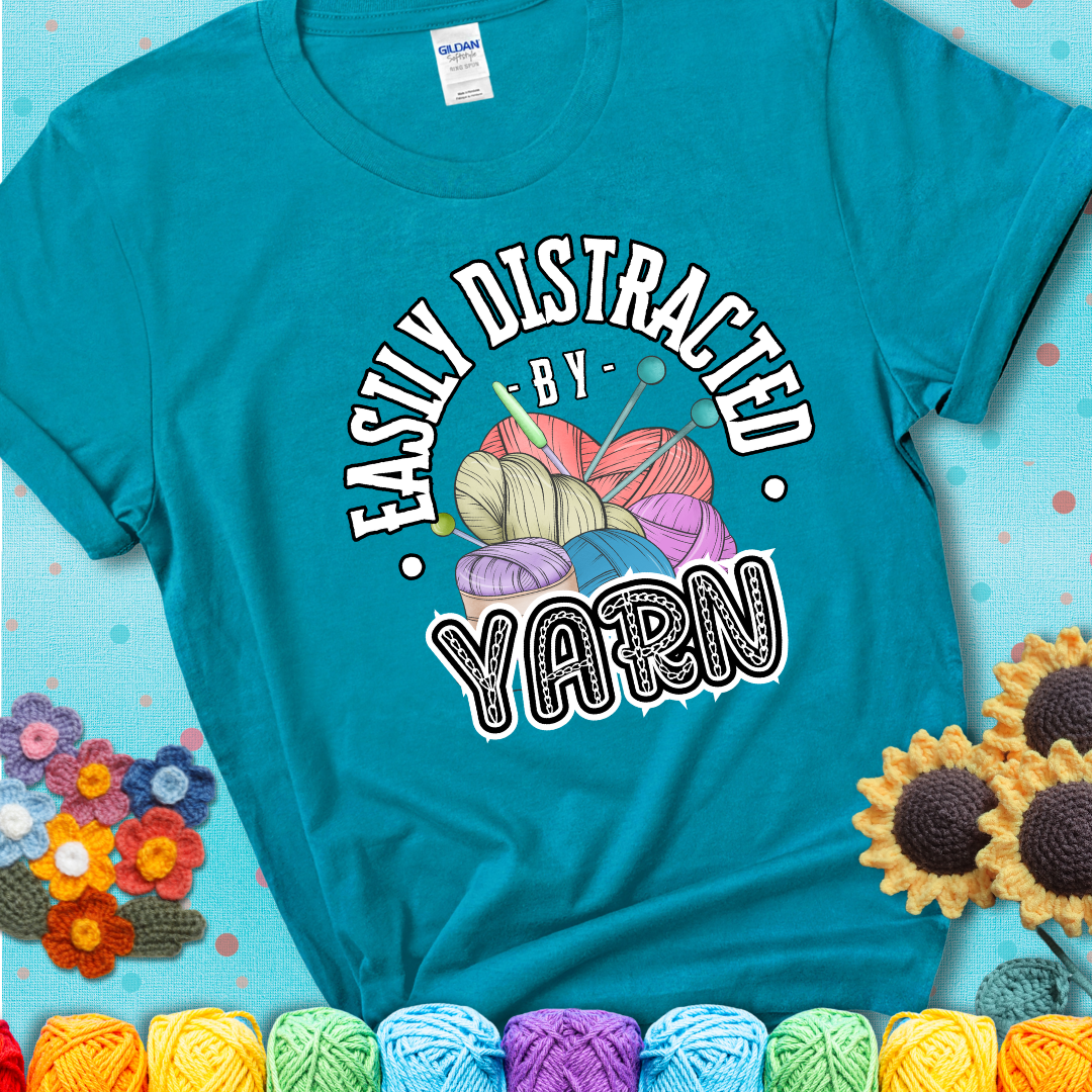 If yarn steals your focus every Design reads 'Easily Distracted By Yarn', perfect crochet gift for yarn lovers; showing a blue-green teal tee with a teal sunflower background