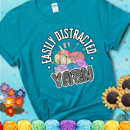 If yarn steals your focus every Design reads 'Easily Distracted By Yarn', perfect crochet gift for yarn lovers; showing a blue-green teal tee with a teal sunflower background