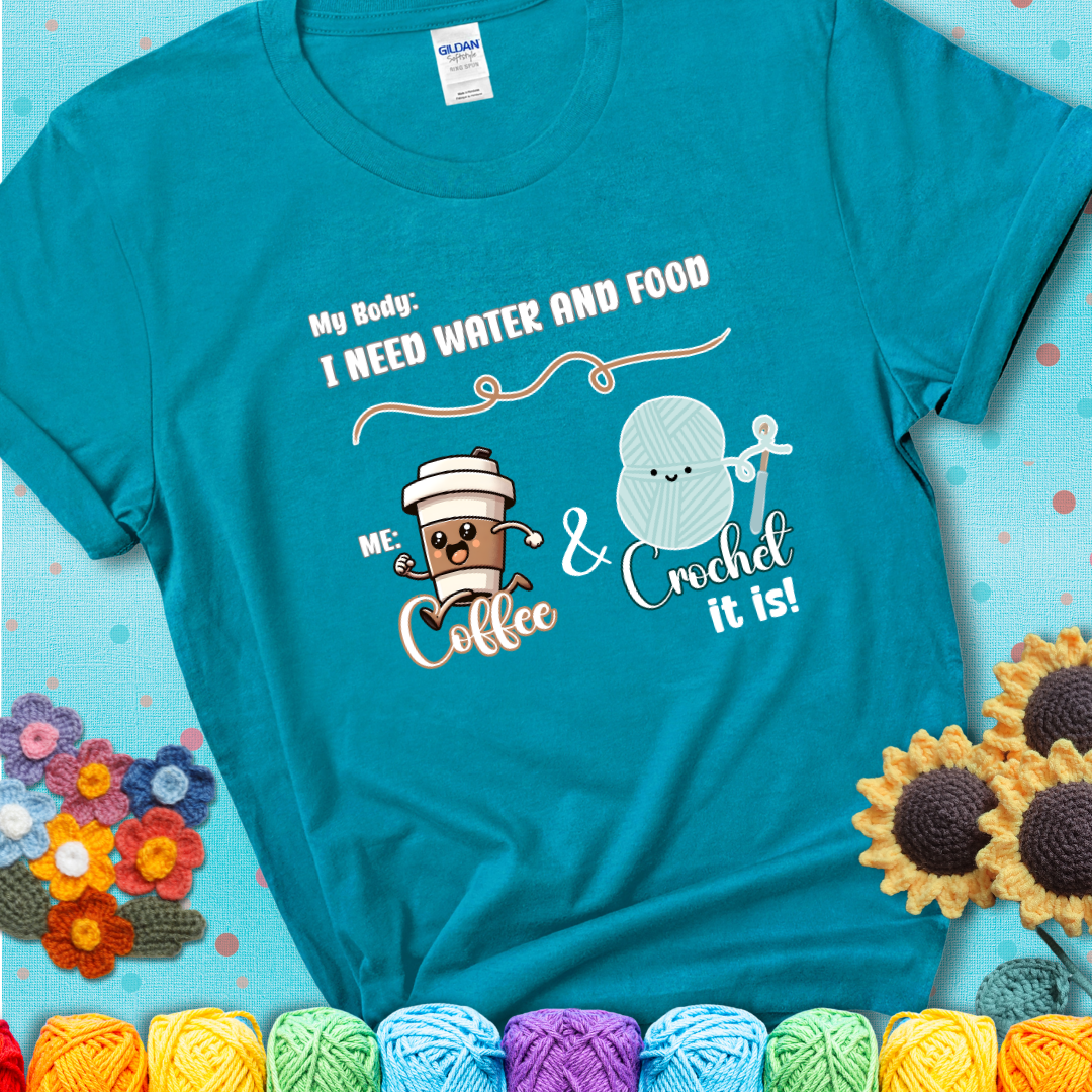 Design reads “My body: I need water and food. Me: Coffee & Crochet it is,” with a smiling coffee cup and yarn ball characters on a teal t-shirt.