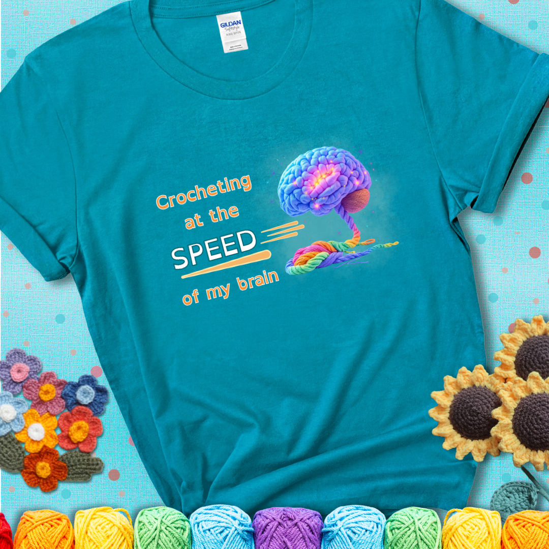 A glowing rainbow brain unravels into colorful yarn with the phrase “Crocheting at the speed of my brain” on a teal t-shirt. 