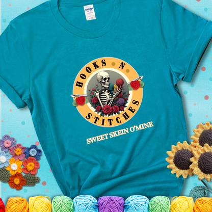 Tropical Blue t-shirt with a skeleton holding colorful yarn, roses, crochet hooks, and the phrases “Hooks ’N Stitches” and “Sweet Skein O’Mine.”