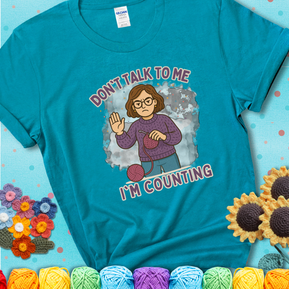 Tropical Blue t-shirt with an annoyed maker holding up a hand beside yarn, with the phrase “Don’t Talk To Me, I’m Counting.”