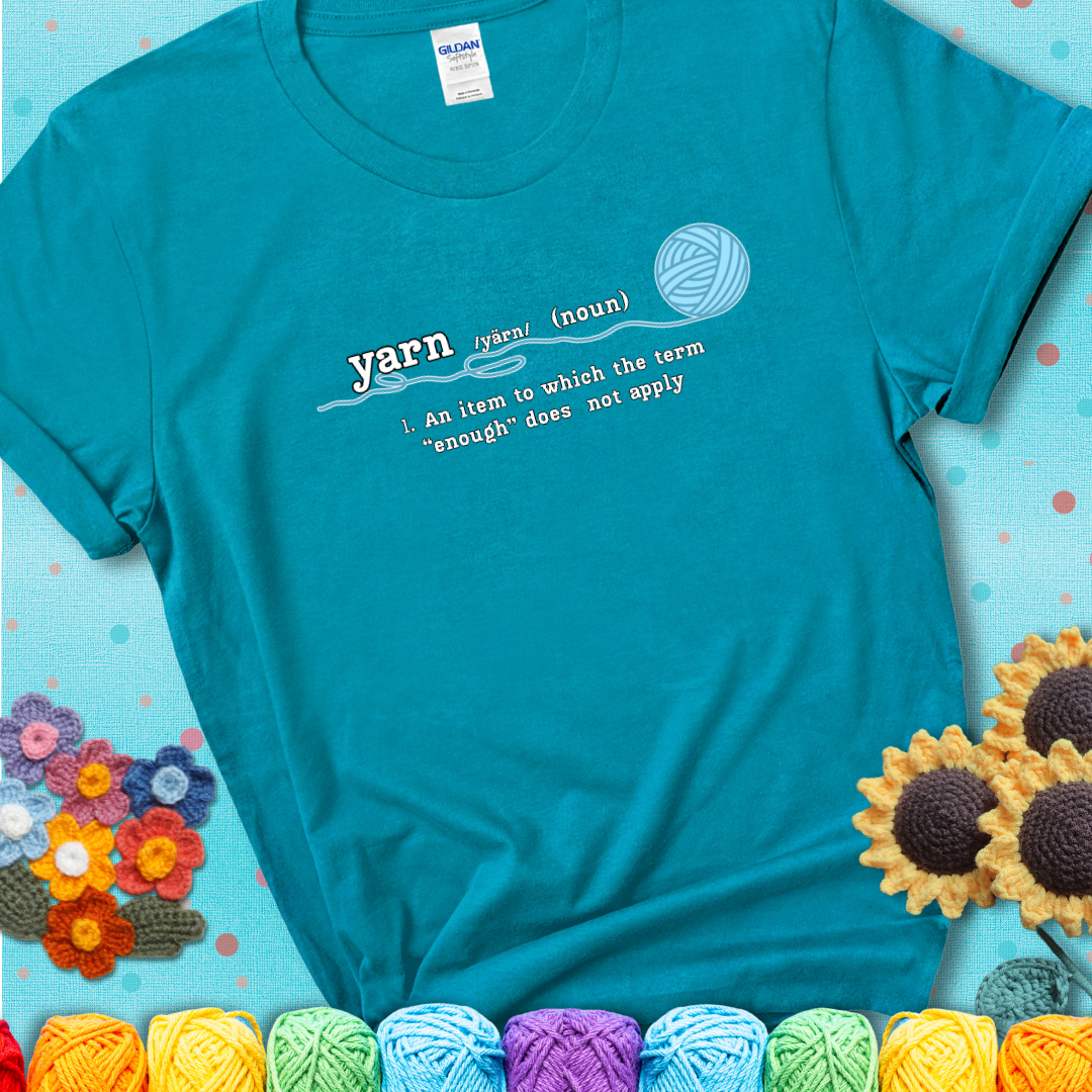 Tropical blue t-shirt with a definition-style yarn graphic reading “An item to which the word ‘enough’ does not apply,” plus a blue ball of yarn with a loose strand.