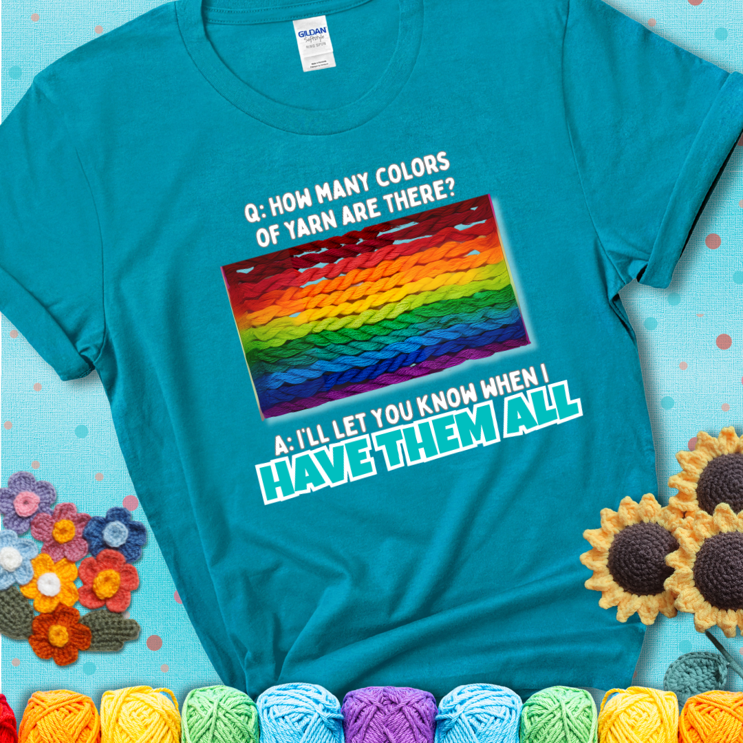 Teal t-shirt with rainbow skeins of yarn stacked in color gradient with playful question: “How many colors of yarn are there?” Answer: “I'll let you know when I have them all.”