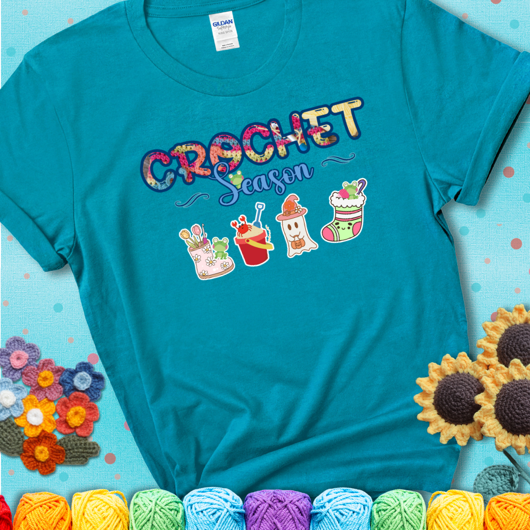 Teal t-shirt shows the words “Crochet Season” with cute seasonal icons below: a spring boot with hooks, summer bucket with crab, fall ghost with pumpkin hat, winter stocking, and tiny frogs.