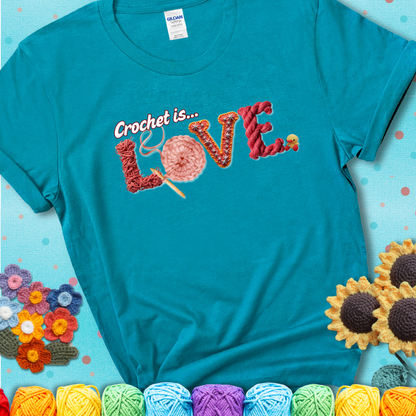 A teal t-shirt featuring the word "LOVE" spelled with different crochet textures and yarn in red tones, with the phrase “Crochet is…” above in script.