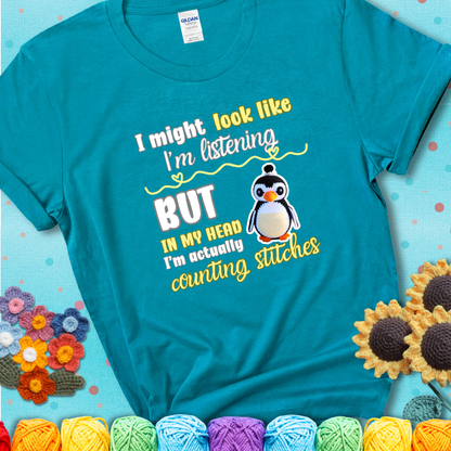Teal t-shirt shows a crocheted penguin next to the text “I might look like I’m listening but in my head I’m actually counting stitches.”
