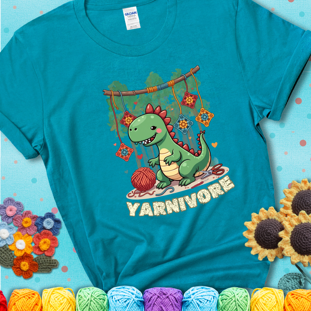 Teal t-shirt shows a cute green dinosaur with yarn ball and granny squares, text “Yarnivore”, a fun crochet shirt for dino and yarn fans.
