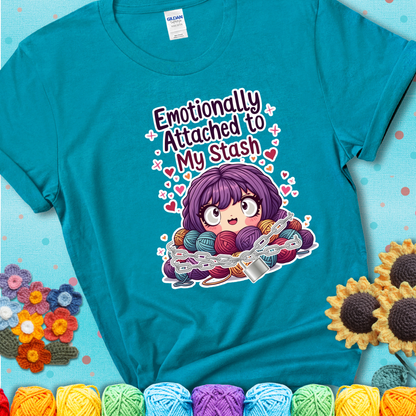 Adorable character with wide eyes hugging a yarn stash wrapped in chains and a lock, with the text “Emotionally Attached to My Stash”  on a blue-green teal tee.