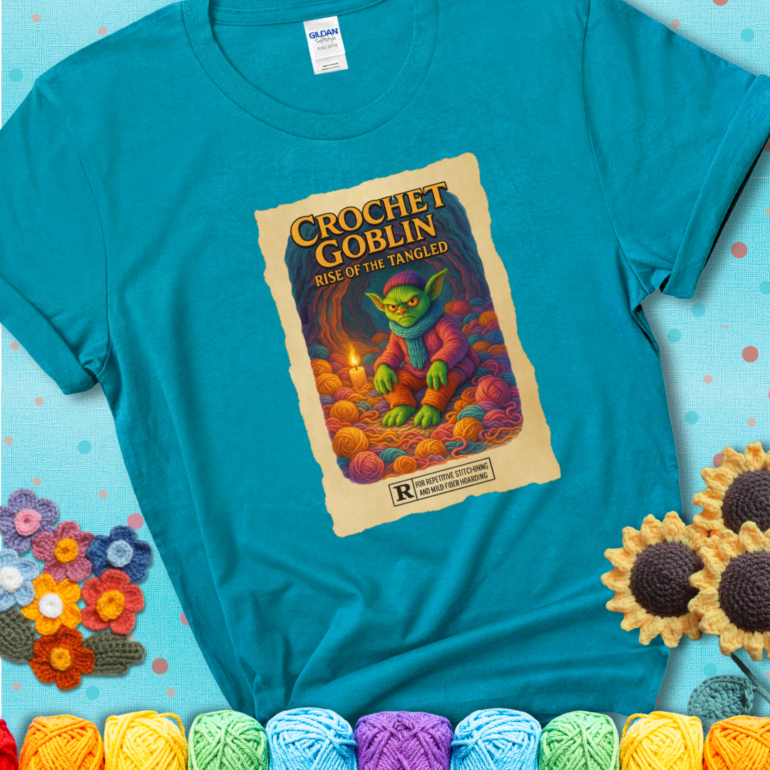 Crochet goblin surrounded by chaotic yarn stash in a cave-like lair. Text reads: “Crochet Goblin: Rise of the Tangled.” A funny fantasy-style teal tee for yarn hoarders and goblin-mode crafters.