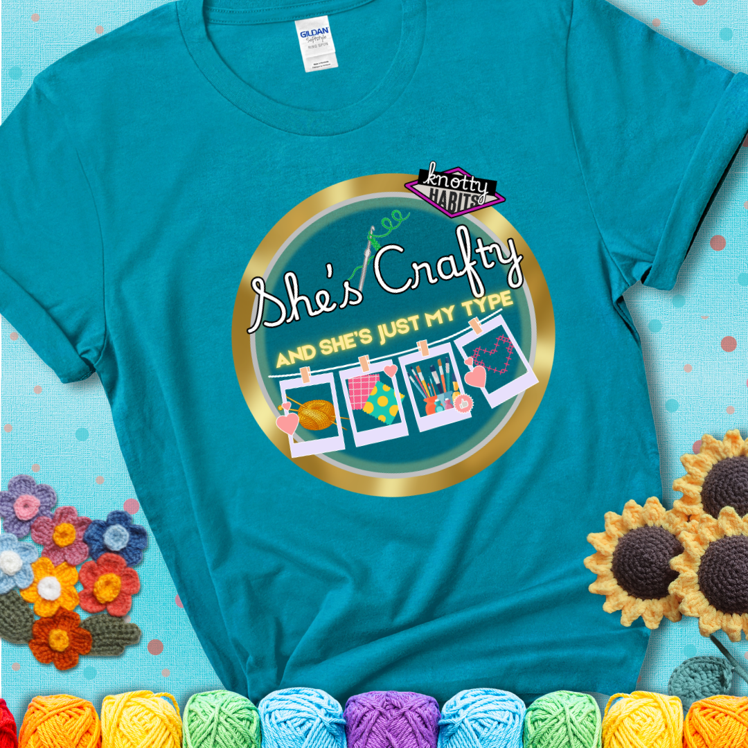 Text on teal tee reads "She’s Crafty & She’s Just My Type" with yarn, fabric, painting, and cross-stitch icons hanging like Polaroids