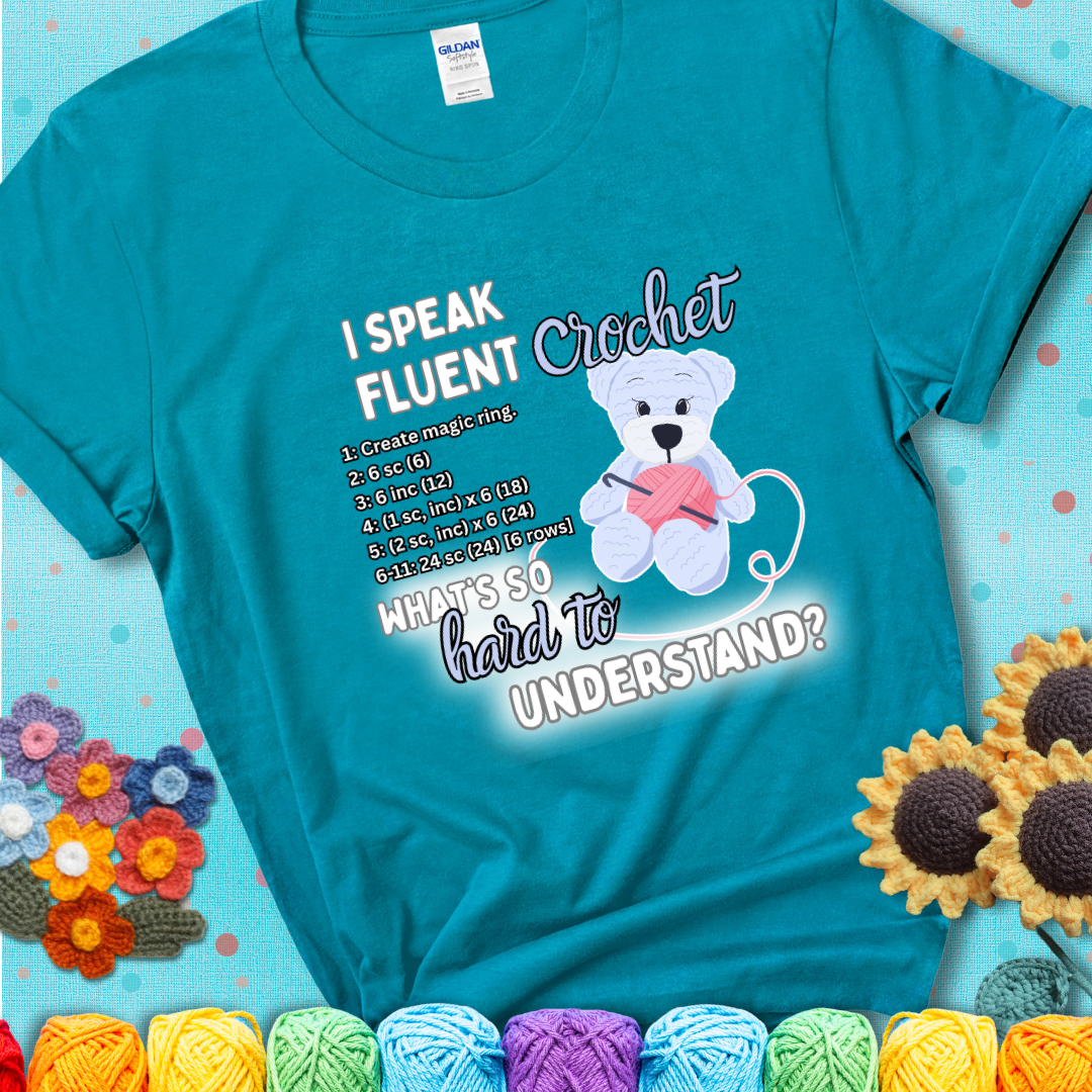 A cute crochet bear holding a yarn ball, surrounded by a short crochet pattern. The phrase reads “I Speak Fluent Crochet – What’s so hard to understand?” on a teal t-shirt.