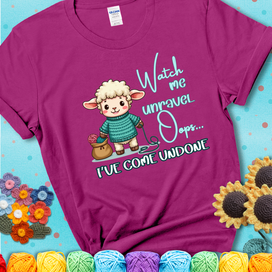 Magenta t-shirt with a cute sheep holding yarn looks startled with the phrase “Watch me unravel… Oops, I’ve come undone.” Perfect mix of whimsy and yarn life chaos.