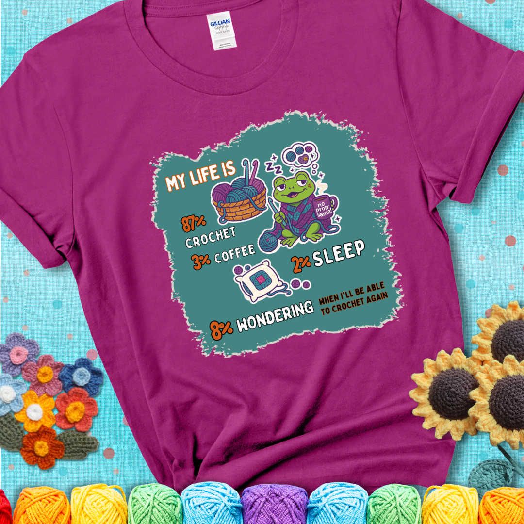 Antique Heliconia t-shirt with a crocheting frog, coffee, yarn, and text showing a playful life breakdown: 87% crochet, 3% coffee, 2% sleep, 8% wondering when to crochet again.