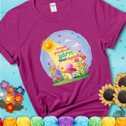Magenta t-shirt featuring a happy spring garden scene with a sunbeam, flowers, and a pink yarn ball on a mushroom, with the quote "Surround yourself with yarn, knot negativity."