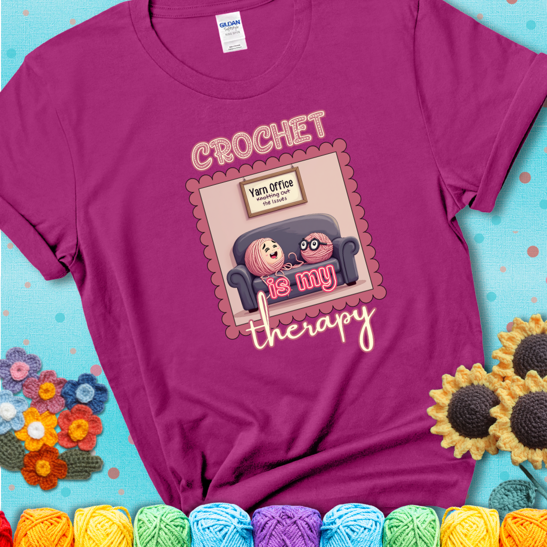 Magenta t-shirt showing a simple text design with yarn cartoon figures. Text reads: “Crochet is My Therapy.” A calming tee for fiber lovers who find healing in every stitch.