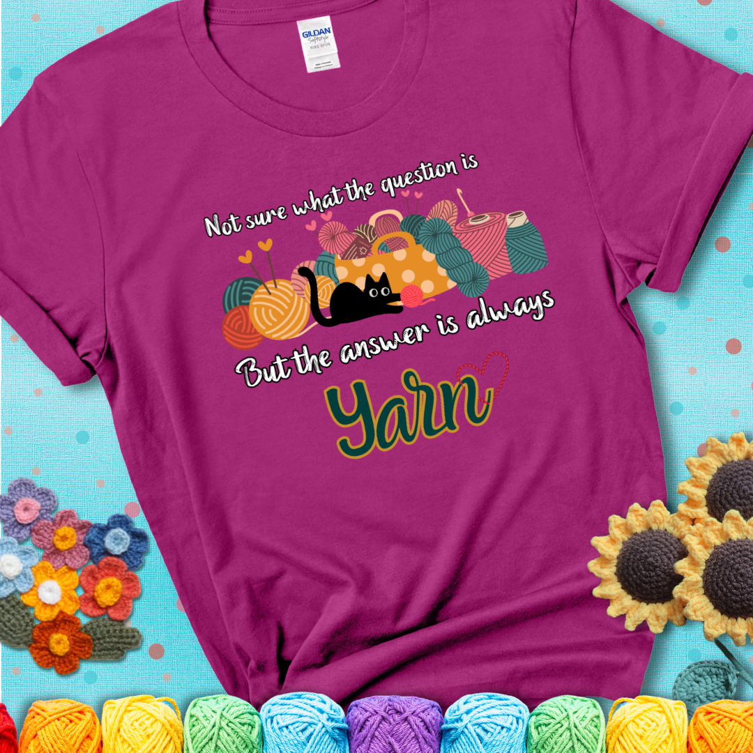 Antique Heliconia t-shirt with a black cat beside a basket of colorful yarn and the phrase, “Not Sure What The Question Was, But The Answer Is Yarn.”