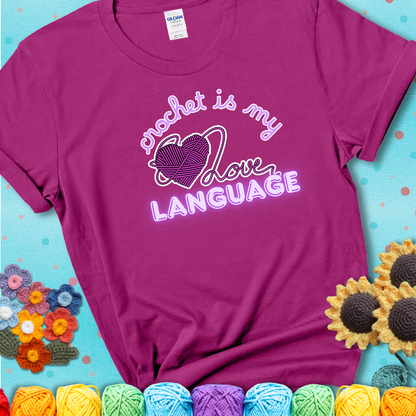 Say it with stitches Design reads 'Crochet Is My Love Language', perfect crochet gift for yarn lovers; showing a magenta tee with a teal sunflower background