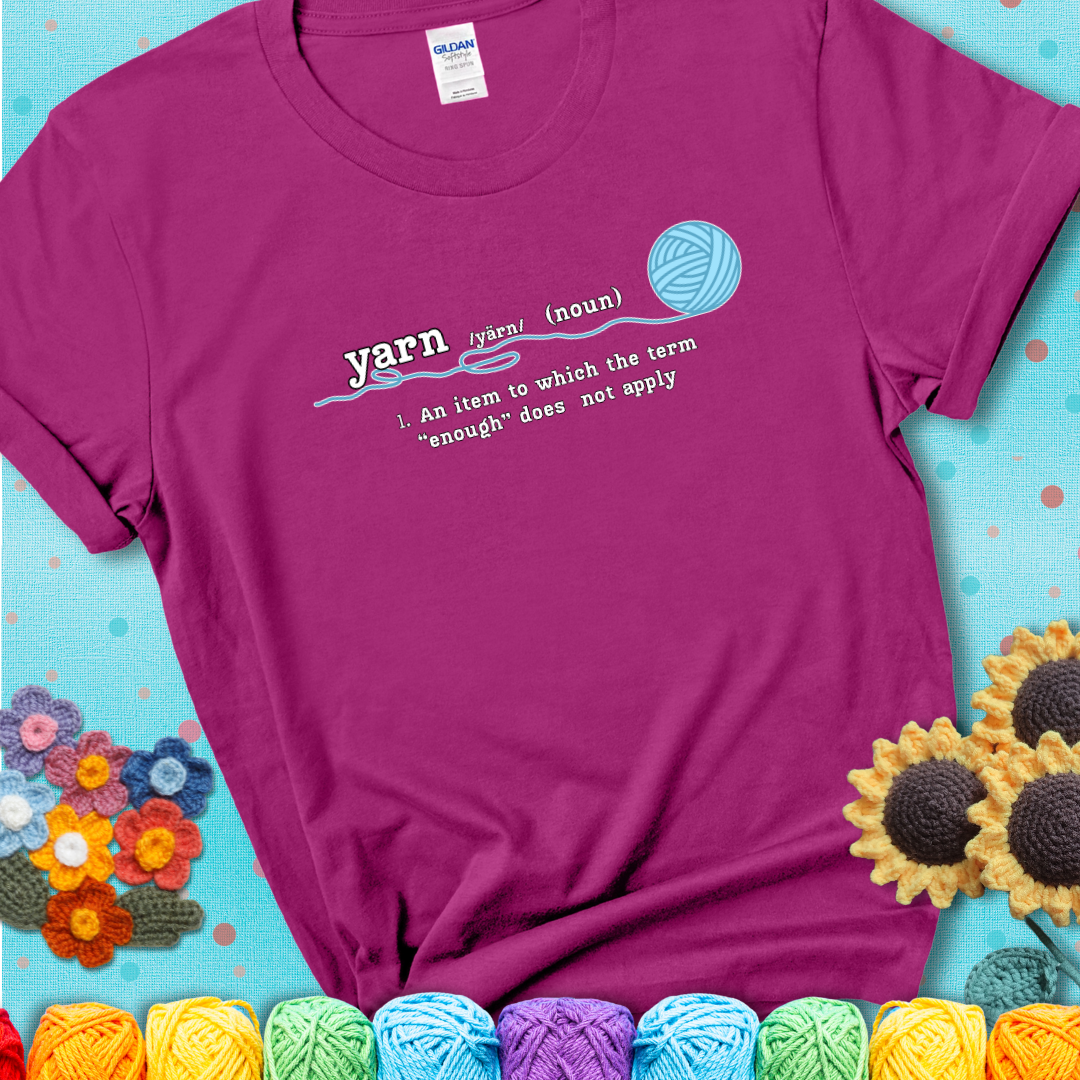 Antique Heliconia t-shirt with a definition-style yarn graphic reading “An item to which the word ‘enough’ does not apply,” plus a blue ball of yarn with a loose strand.
