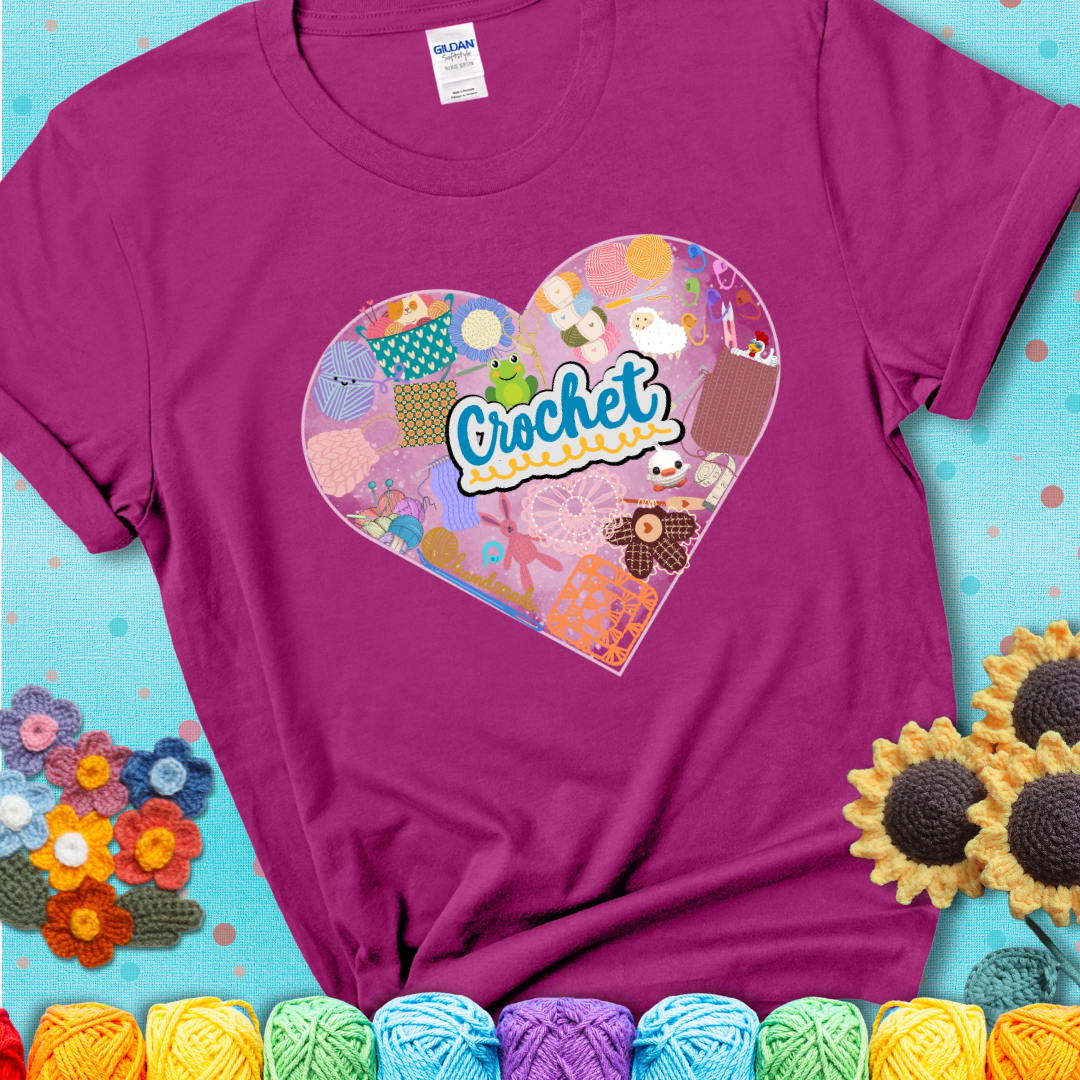 A heart filled with colorful crochet essentials including yarn, hooks, scissors, notions, and handmade items, with the word "Crochet" prominently in the center of a magenta t-shirt.