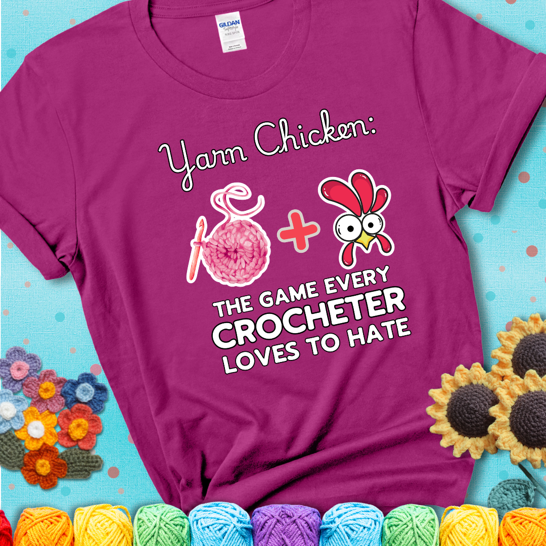 Cartoon chicken inside a yarn ball with crochet circle background. Text reads: “Yarn Chicken: The Game Every Crocheter Loves to Lose.” A fun and relatable tee for fiber artists who like to live on the edge, showing a magenta tee with a teal sunflower background
