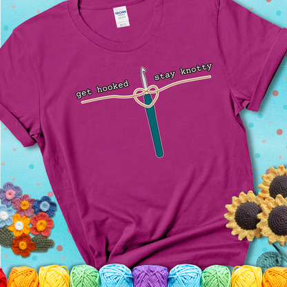 Hooked on yarn? Same Design reads 'Get Hooked, Stay Knotty' , perfect crochet gift for yarn lovers, showing a magenta tee with a teal sunflower background