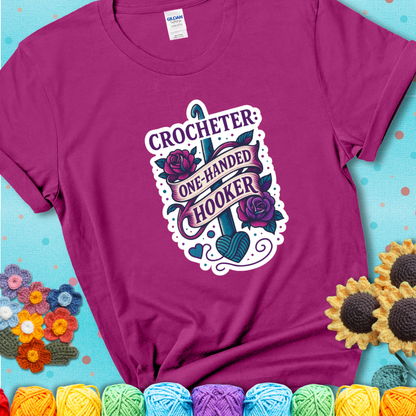 Antique Heliconia t-shirt with a tattoo-style crochet design featuring a crochet hook, roses, and the phrase “Crocheter: One-Handed Hooker.”