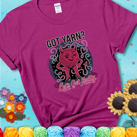 Antique Heliconia t-shirt with a cheeky pink yarn ball wearing devil horns, arms, and legs, winking beneath the phrase “Got Yarn? Let’s Get Knotty