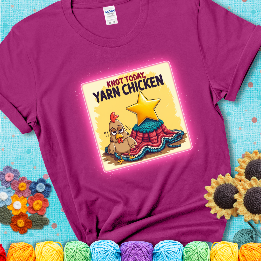 A magenta t-shirt showing a frazzled cartoon chicken stands next to a nearly-finished project with minimal yarn left, with the phrase “Knot Today, Yarn Chicken” above.