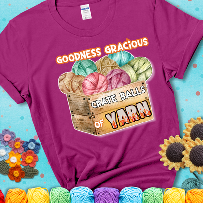 Wooden crate filled with colorful yarn balls and bold text “Goodness Gracious, Crate Balls of Yarn” with flame effects, a funny gift for crocheters showing a magenta tee with a teal sunflower background