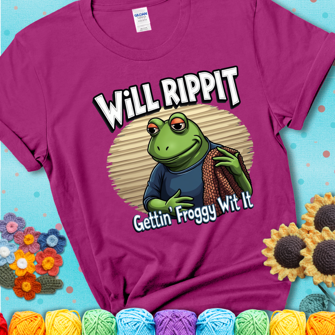 Cool frog holding a yarn blanket. Text reads: “Will Rippit Gettin’ Froggy Wit It.” A hip and humorous crochet magenta tee for yarn lovers with rhythm.