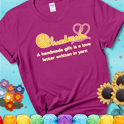 Soft script-style design with heart detail. Text reads: “A Handmade Gift Is a Love Letter Written in Yarn.” A sweet and sentimental shirt for crocheters who craft from the heart, showing a magenta tee with a teal sunflower background