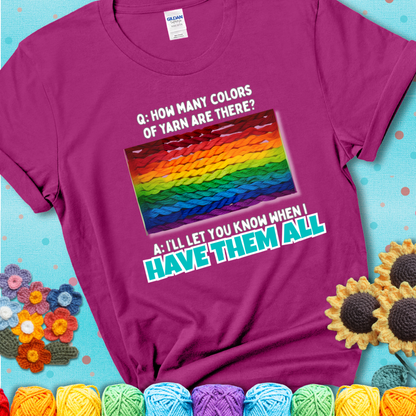 Magenta t-shirt with rainbow skeins of yarn stacked in color gradient with playful question: “How many colors of yarn are there?” Answer: “I'll let you know when I have them all.”