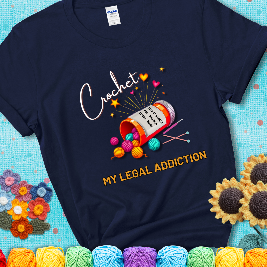 Navy t-shirt with a prescription bottle spilling colorful yarn balls, small crochet details, and the phrase “Crochet: My Legal Addiction.”