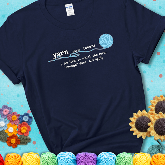 Navy blue t-shirt with a definition-style yarn graphic reading “An item to which the word ‘enough’ does not apply,” plus a blue ball of yarn with a loose strand.
