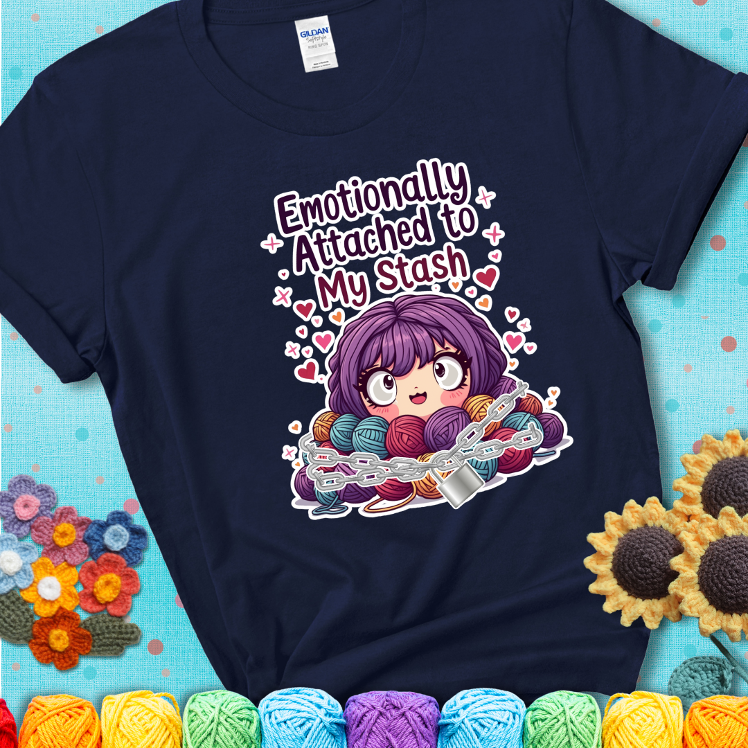 Adorable character with wide eyes hugging a yarn stash wrapped in chains and a lock, with the text “Emotionally Attached to My Stash”  on a navy blue tee.